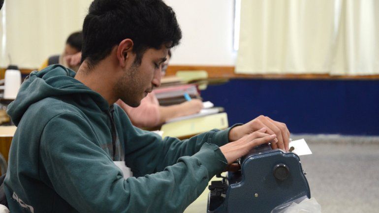 Carlos Tapia en el aula de la facultad con su vieja máquina que escribe en braille y con su nueva notebook. 