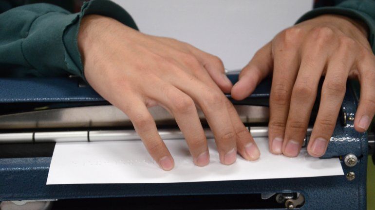 Carlos Tapia en el aula de la facultad con su vieja máquina que escribe en braille y con su nueva notebook. 