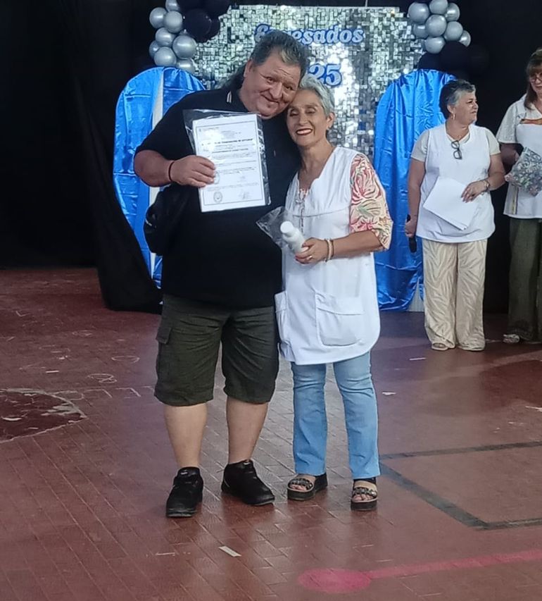 El trabajador municipal Domingo Hernán Martínez concluyó la escuela primaria y se lo ve feliz por el logro. Junto a él, también feliz se observa a la docente Gloria Díaz.