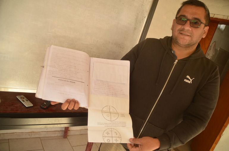 Gonzalo Rivas sostiene el cuaderno de un adulto mayor que no sabía leer ni escribir y que obtuvo las mejoras calificaciones por el aprendizaje y finalización de sus estudios primarios. El cuaderno destaca por el cuidado y la aplicación del alumno. 